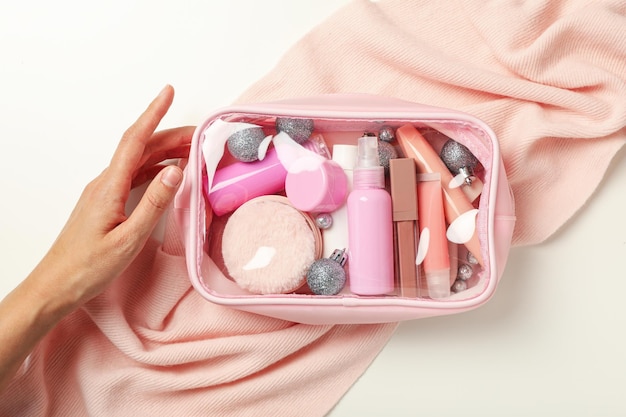 Bolas de cosméticos cachecol em bolsa cosmética e mão na vista superior de fundo branco