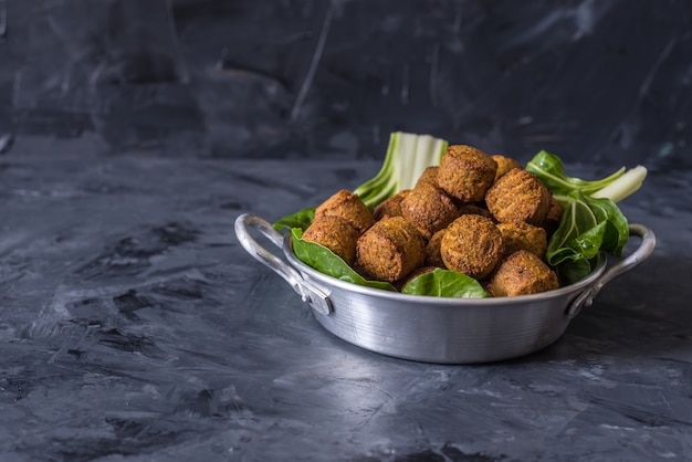 bolas de falafel servidas em chapa com verde folhas sobre fundo preto de madeira