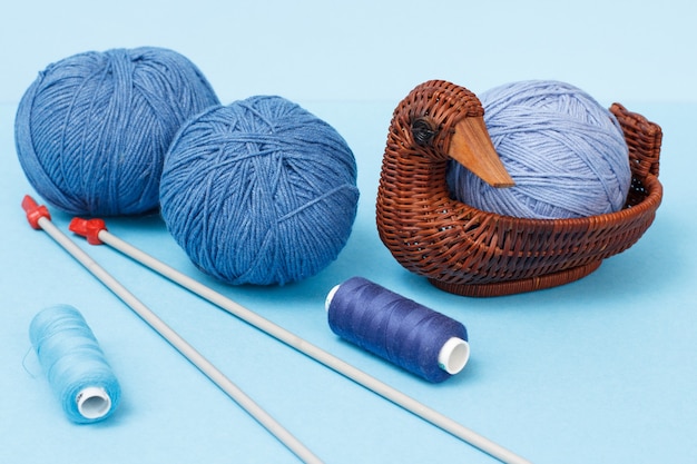 Bolas de fio de tricô, agulhas de tricô de metal, fios e cesta de vime sobre um fundo azul. Conceito de tricô.