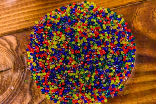 Bolas de hidrogel multicoloridas em uma tigela de vidro na mesa de madeira Vista superior