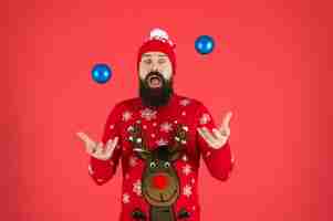 Foto bolas de malabarismo atividades festivas divertidas hipster alegre homem barbudo usa suéter de inverno e chapéu segura bolas fundo vermelho conceito de ano novo festa de natal roupa de inverno decorações de inverno