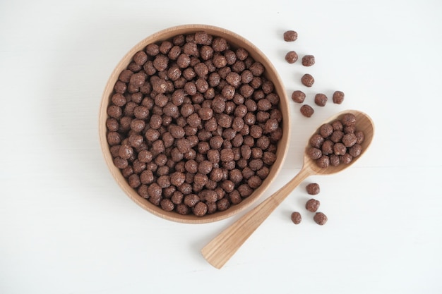 Bolas de milho de chocolate em uma tigela de madeira e colher espalhadas em um fundo branco para texto