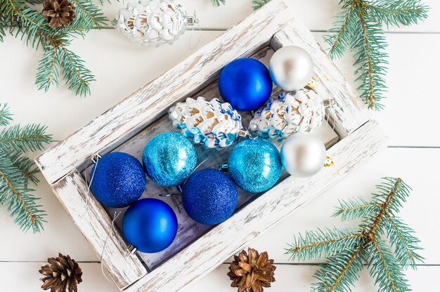 Bolas de Natal azuis e prateadas em uma caixa de madeira com fundo branco de madeira. vista do topo.