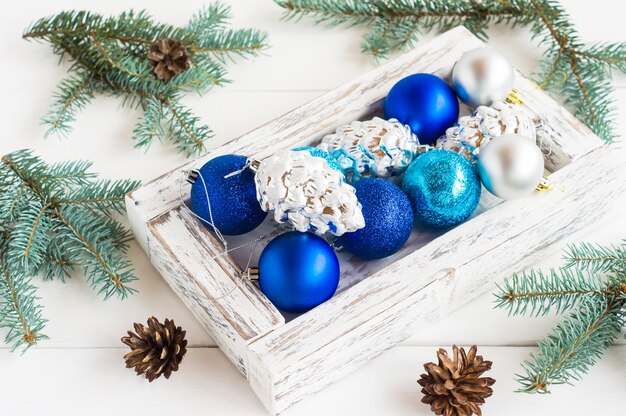 Bolas de Natal brilhantes em uma caixa de madeira branca em uma composição com ramos de abeto e cones.