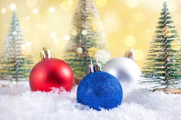 Bolas de Natal coloridas na neve entre as árvores de Natal de brinquedo. Bokeh com luzes. Lindo cartão de Natal.