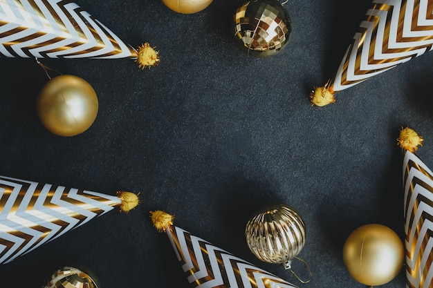 Bolas de natal douradas e bonés de festa, em um fundo preto.