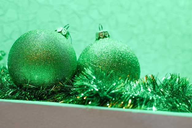 Bolas de Natal verdes brilhantes caídas sobre enfeites verdes, close-up com iluminação verde