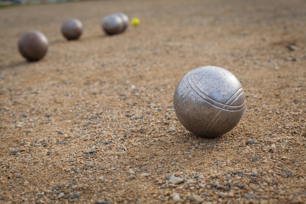 Bolas de petanca em um campo de areia com outra bola de metal no fundo