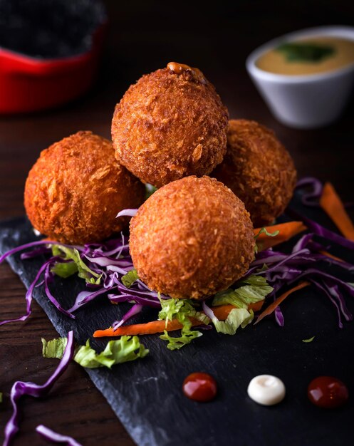 Bolas de queijo com cenoura de cebola e folha de alface servidas em prato isolado em mesa de madeira vista lateral da comida árabe