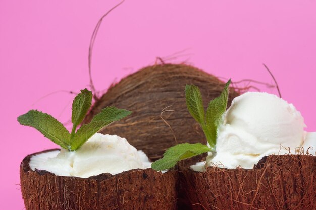 Bolas de sorvete de baunilha em metades de coco fresco, decoradas com folhas de hortelã em um fundo rosa.