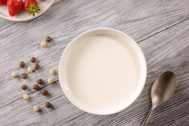 Bolas de diferentes granos y un plato de leche y una fresa madura sobre una mesa de madera gris con espacio de copia. Desayuno por la mañana. Vista superior