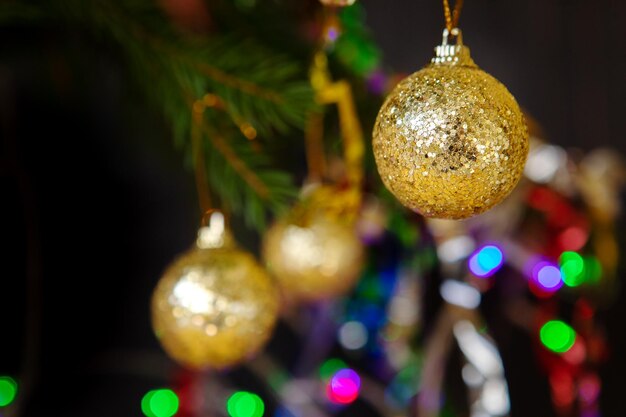 Bolas doradas de árbol de Navidad en una rama en un fondo oscuro luces de guirnaldas en el fondo