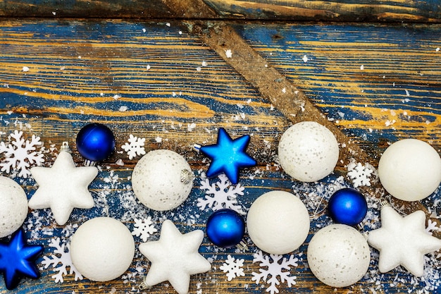 Bolas e estrelas de Natal brancas e azuis, flocos de neve e glitter espalhado com neve artificial. Tábuas de madeira vintage em tons de azul, vista superior