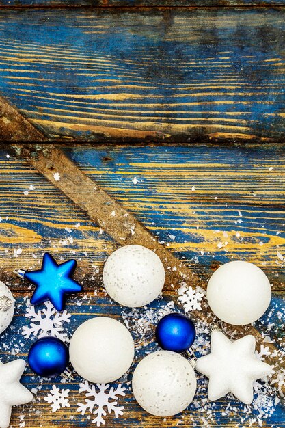 Bolas e estrelas de Natal brancas e azuis, flocos de neve e glitter espalhado com neve artificial. Tábuas de madeira vintage em tons de azul, vista superior