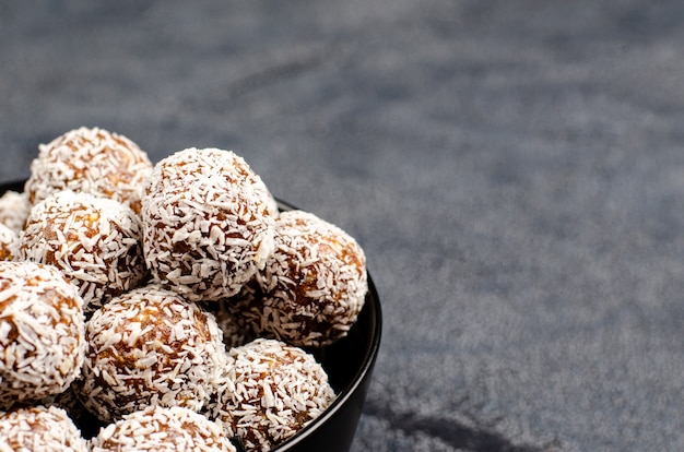 Bolas energéticas de dátiles, maní, miel, avena en un tazón negro, plano