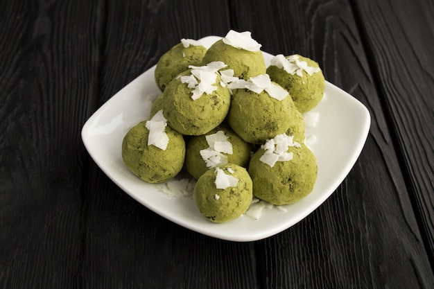 Bolas energéticas con polvo de matcha y chips de coco en el plato blanco sobre madera negra