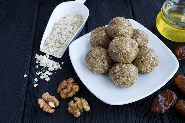 Foto bolas de energía con nueces, cereales de avena, dátiles y miel en la placa blanca.