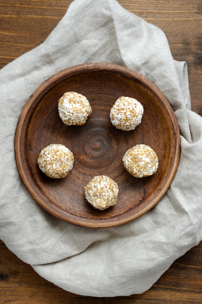 Bolas de energía veganas crudas caseras en virutas de coco en placa de cerámica en la mesa de madera vieja