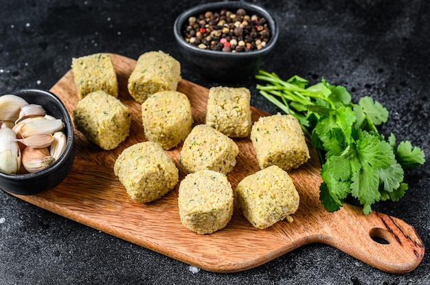 Bolas de falafel crudo sobre una tabla de cortar de madera.