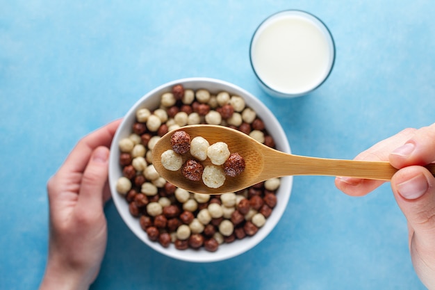 Bolas glaseadas de chocolate, marrón y blanco y un vaso de leche para un desayuno seco y saludable. Vista superior. Cereales cuchara y tazón en manos