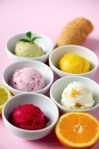 Bolas de helado rojas, moradas, amarillas, verdes, en cuencos, conos de waffle, bayas, naranja, mango, limón, menta, pistacho
