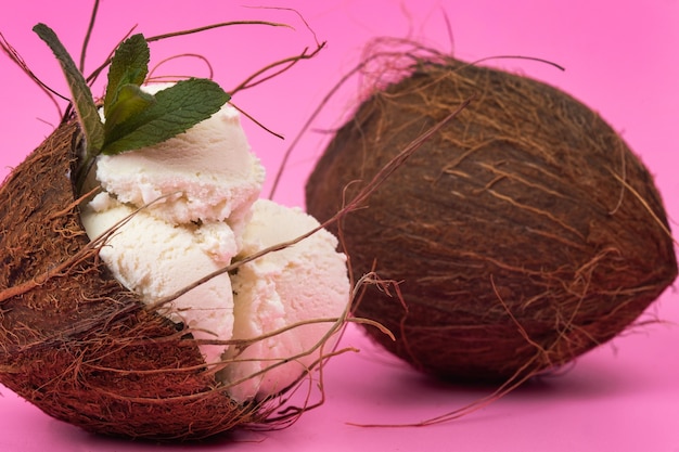 Bolas de helado de vainilla en un coco vacío decorado con hojas de menta sobre un fondo rosa