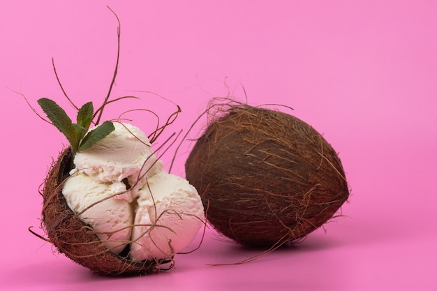 Bolas de helado de vainilla en un coco vacío decorado con hojas de menta sobre un fondo rosa