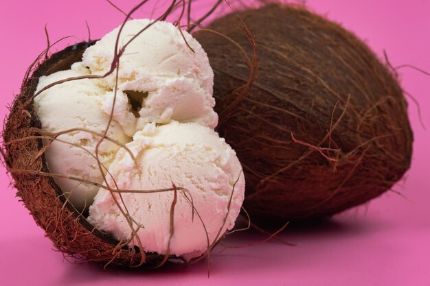 Bolas de helado de vainilla en un coco vacío decorado con hojas de menta sobre un fondo rosa