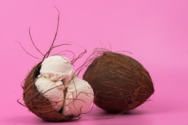 Bolas de helado de vainilla en un coco vacío decorado con hojas de menta sobre un fondo rosa.