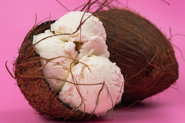 Bolas de helado de vainilla en un coco vacío decorado con hojas de menta sobre un fondo rosa.