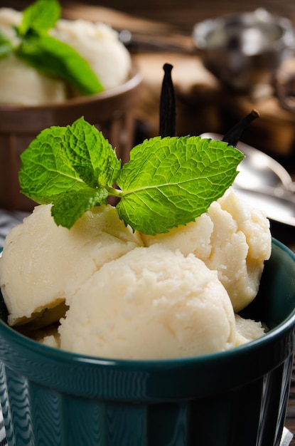 Bolas de helado de vainilla en cuencos de arcilla sobre una mesa de cocina de madera con una bola de helado a un lado