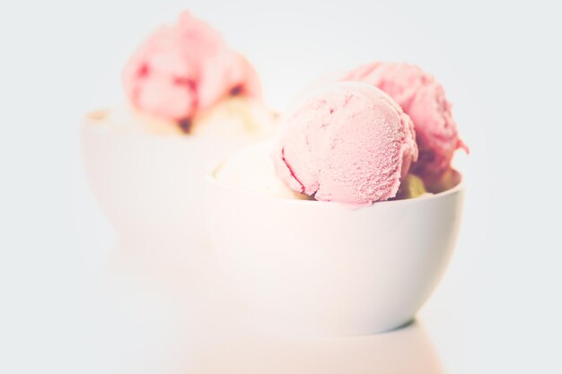 Foto bolas de helado de vainilla y fresa en una taza blanca.