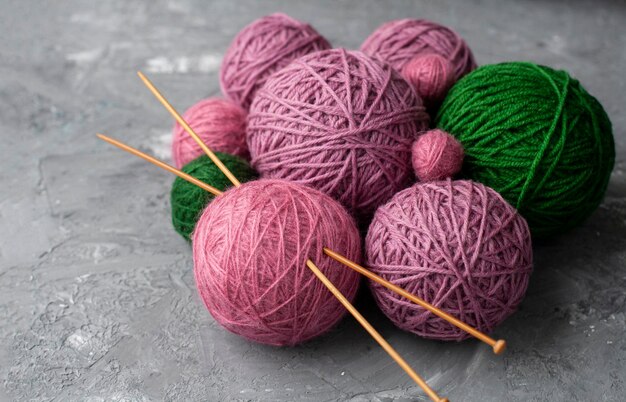 Bolas de hilo rosa púrpura y verde con agujas de tejer de madera en bola rosa sobre fondo gris