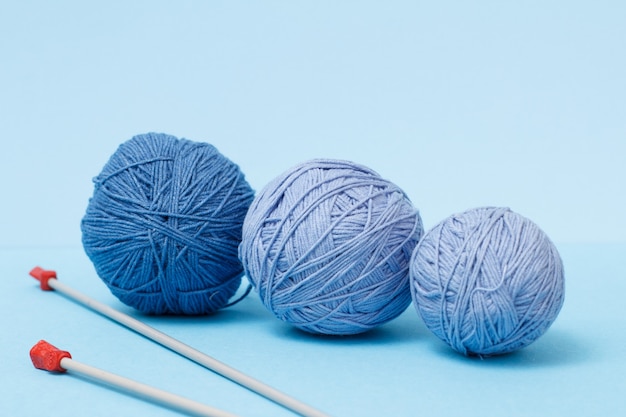 Bolas de hilo de tejer y agujas de tejer de metal sobre un fondo azul. Concepto de tejido.