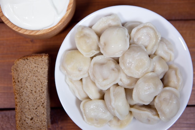 Bolas de masa hervida rusas tradicionales con crema agria en un primer plano de fondo de madera