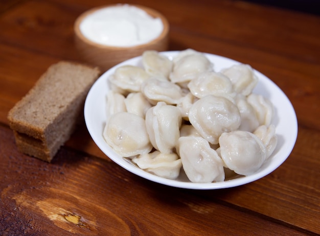 Bolas de masa hervida rusas tradicionales con crema agria en un primer plano de fondo de madera