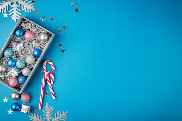 Bolas de Navidad azul, rosa y plata, cuentas de Navidad plateadas en una caja de madera y bastones de caramelo en azul. Endecha plana. Borde festivo para tarjeta de felicitación