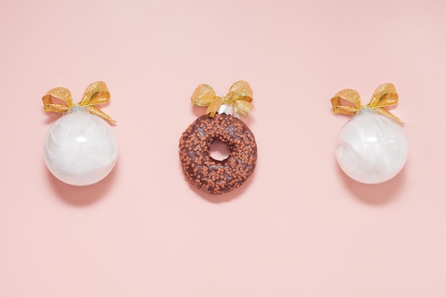 Bolas de navidad blancas con donas y lazos dorados decoración creativa de año nuevo sobre fondo rosa