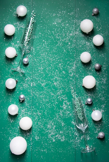 Bolas de Navidad blancas y grises con copas de champán se encuentran sobre un fondo de madera verde