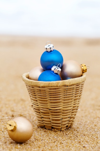 Bolas de Navidad en una canasta en la orilla arenosa del océano