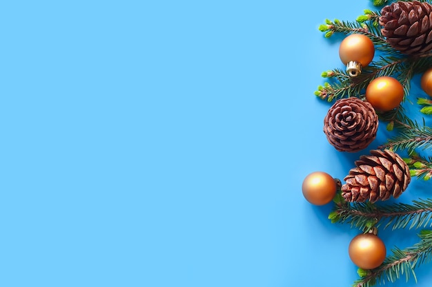 Bolas de Navidad doradas, ramas de abeto y piñas sobre fondo azul.