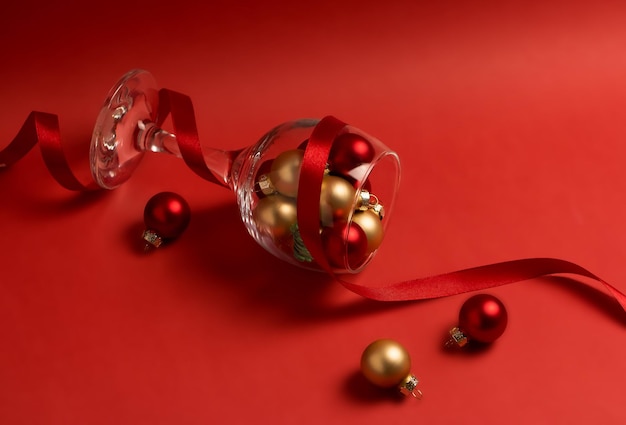 Bolas de Navidad doradas y rojas en una copa de vino decorada con cinta de seda roja sobre un fondo rojo
