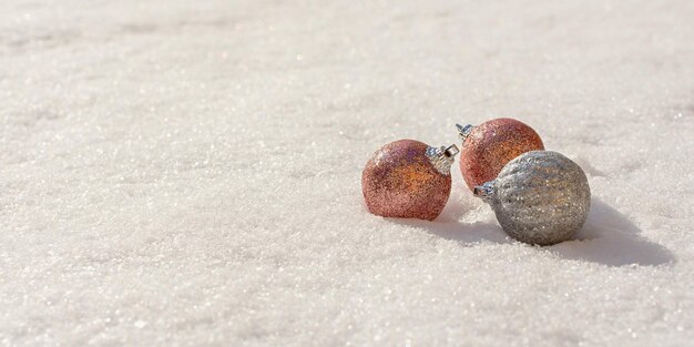 Bolas de Navidad nieve. Las decoraciones navideñas plateadas y rosas brillantes yacen en la nieve y brillan