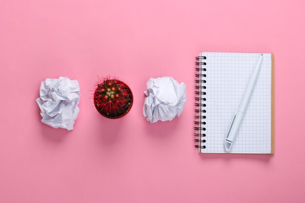 Bolas de papel arrugado, maceta de cactus y bloc de notas en rosa pastel. Espacio de trabajo