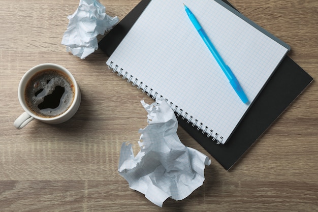 Bolas de papel, cuaderno, taza de café y bolígrafo sobre mesa de madera, vista superior