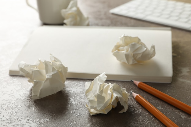 Bolas de papel, cuaderno, taza de café, teclado y lápices sobre fondo gris, de cerca