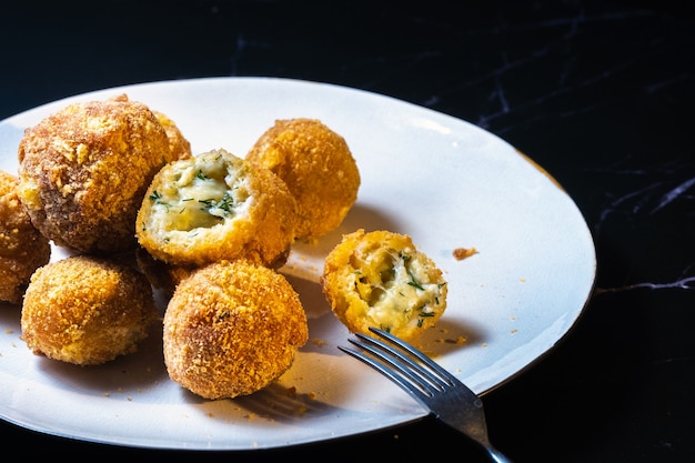 Bolas de queso con eneldo en el interior para un aperitivo en un plato sobre un fondo negro.