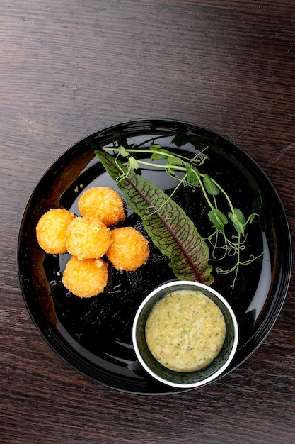 Bolas de queso con salsa de miel y mostaza en un plato negro brillante