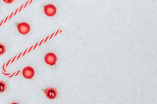 Bolas rojas y bastones de caramelo se encuentran en la nieve.