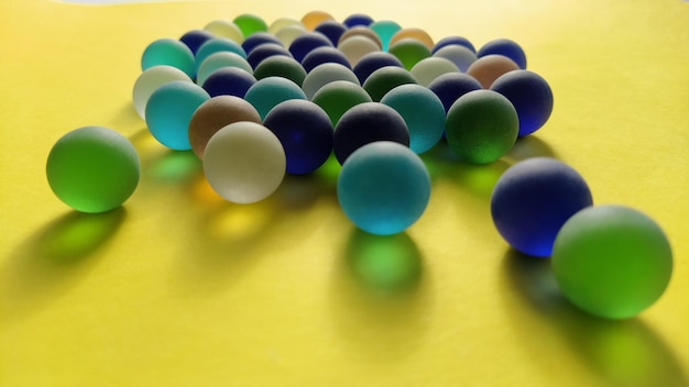 Bolas de vidrio de diferentes colores yacen sobre una superficie amarilla 2 bolas están contra todas las demás
